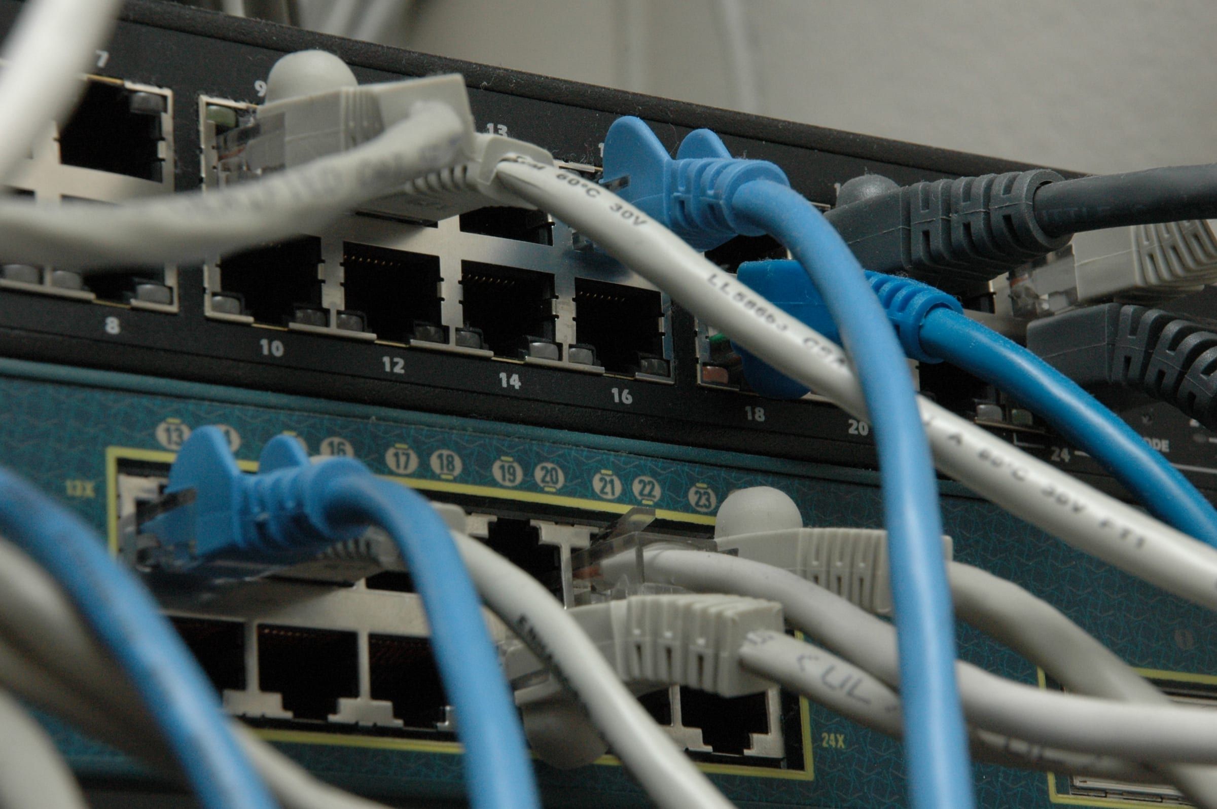 Blue and grey ethernet cables plugged into the ports of two rack-mounted network switches, seen close up.